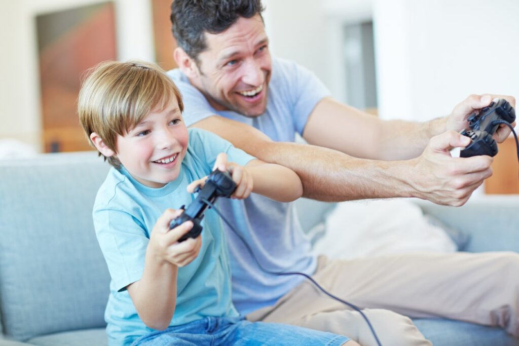 A dad playing a racing game on the PlayStation with his young son